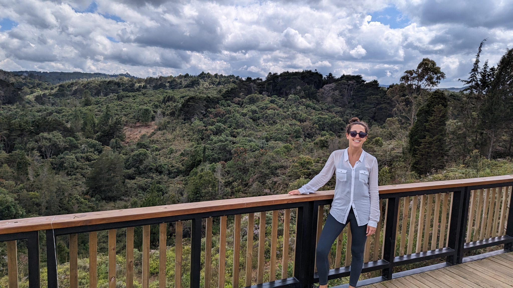 A young woman standing on a wooden platform in front of a large forest in Colombia.
